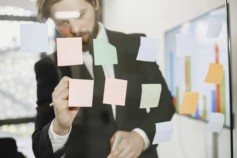 Manager scrive su post it appiccicati su una parte di vetro per disegnare la Value Stream Mapping | Menti Pratiche 